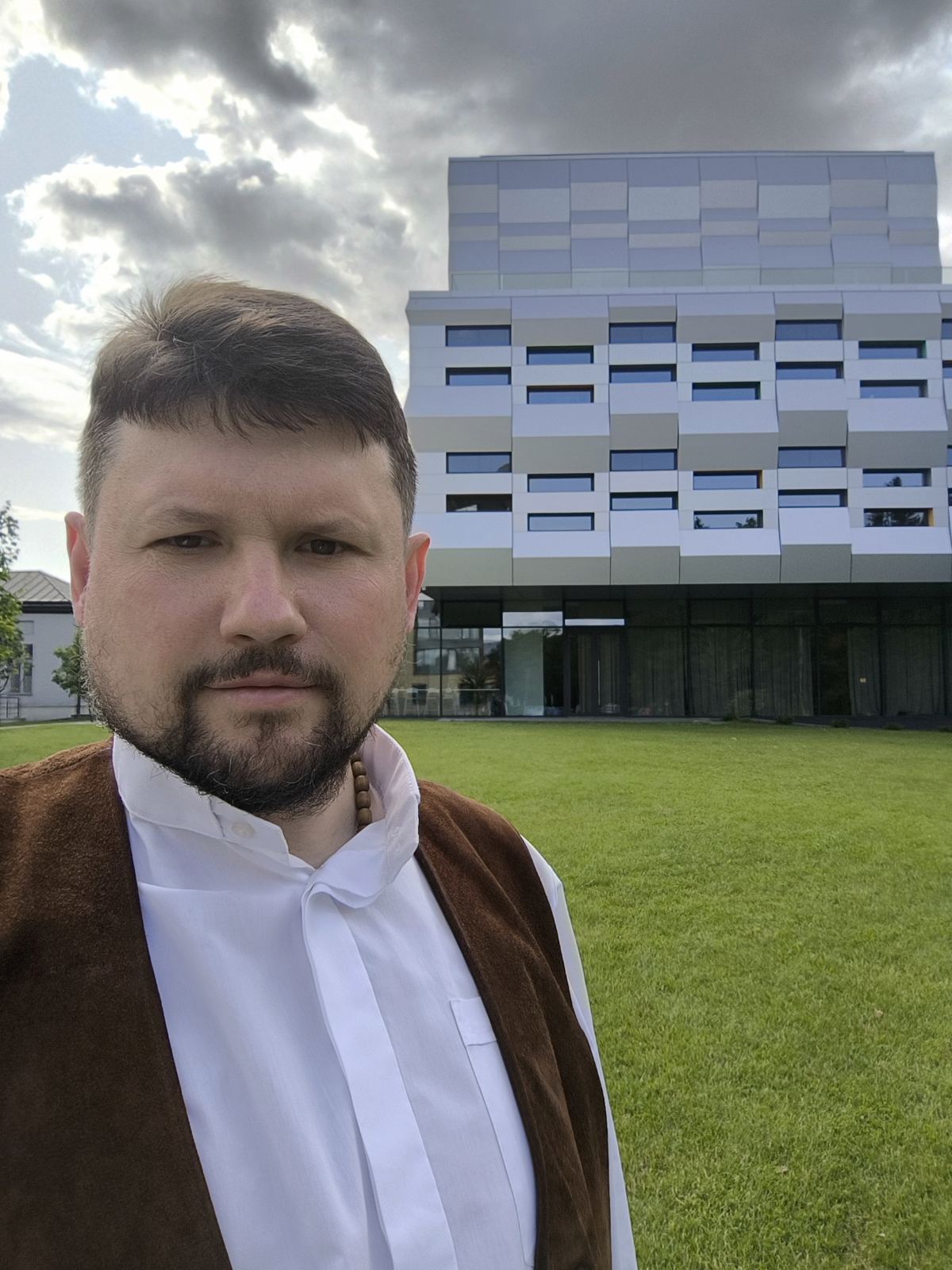Чоловік перед сучасною будівлею та зеленою галявиною